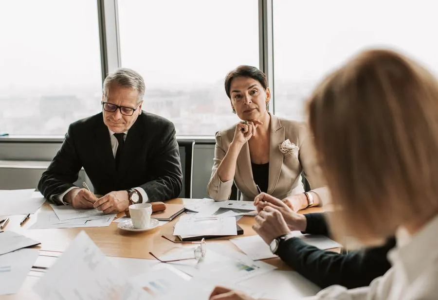 Trois professionnels autour d’une table de réunion couverte de documents, deux d’entre eux écoutant avec attention